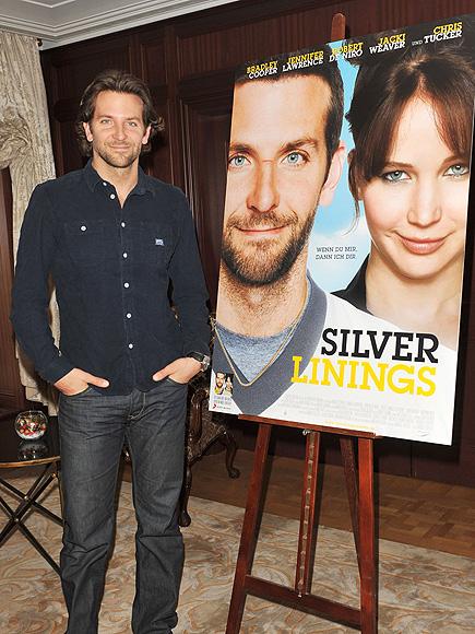 BRADLEY COOPER LOOKING COOL STANDING NEXT TO THE MOVIE POSTER "SILVER LININGS". 