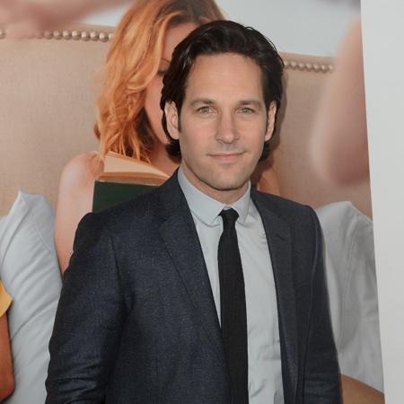 ACTOR PAUL RUDD WEARING A SUIT AND STANDING IN FRONT OF THE MOVIE POSTER FOR THIS IS 40. 