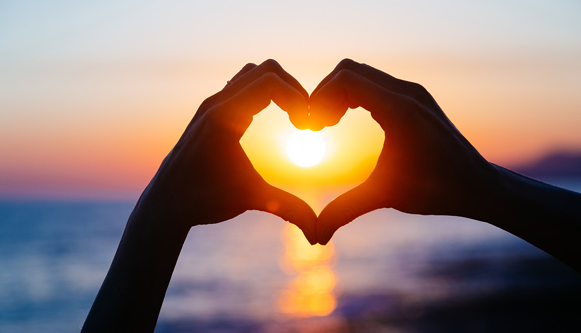 hands forming a heart shape with sunset silhouette. Copy space text.