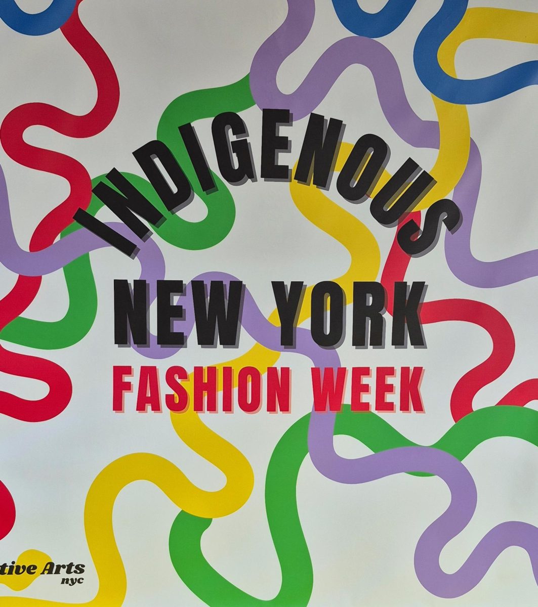 Sign reads “Indigenous New York Fashion Week” in black and red on the words. The background is white with squiggled lines in red, green, yellow, and lavender intersecting behind the words. 
