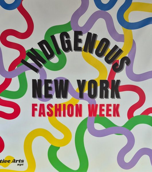 Sign reads “Indigenous New York Fashion Week” in black and red on the words. The background is white with squiggled lines in red, green, yellow, and lavender intersecting behind the words. 